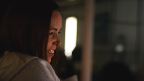 Close-Up-Of-Smiling-Woman-Sitting-On-Sofa-At-Home-At-Night-Streaming-Or-Watching-Movie-Or-Show-On-Laptop-Or-TV